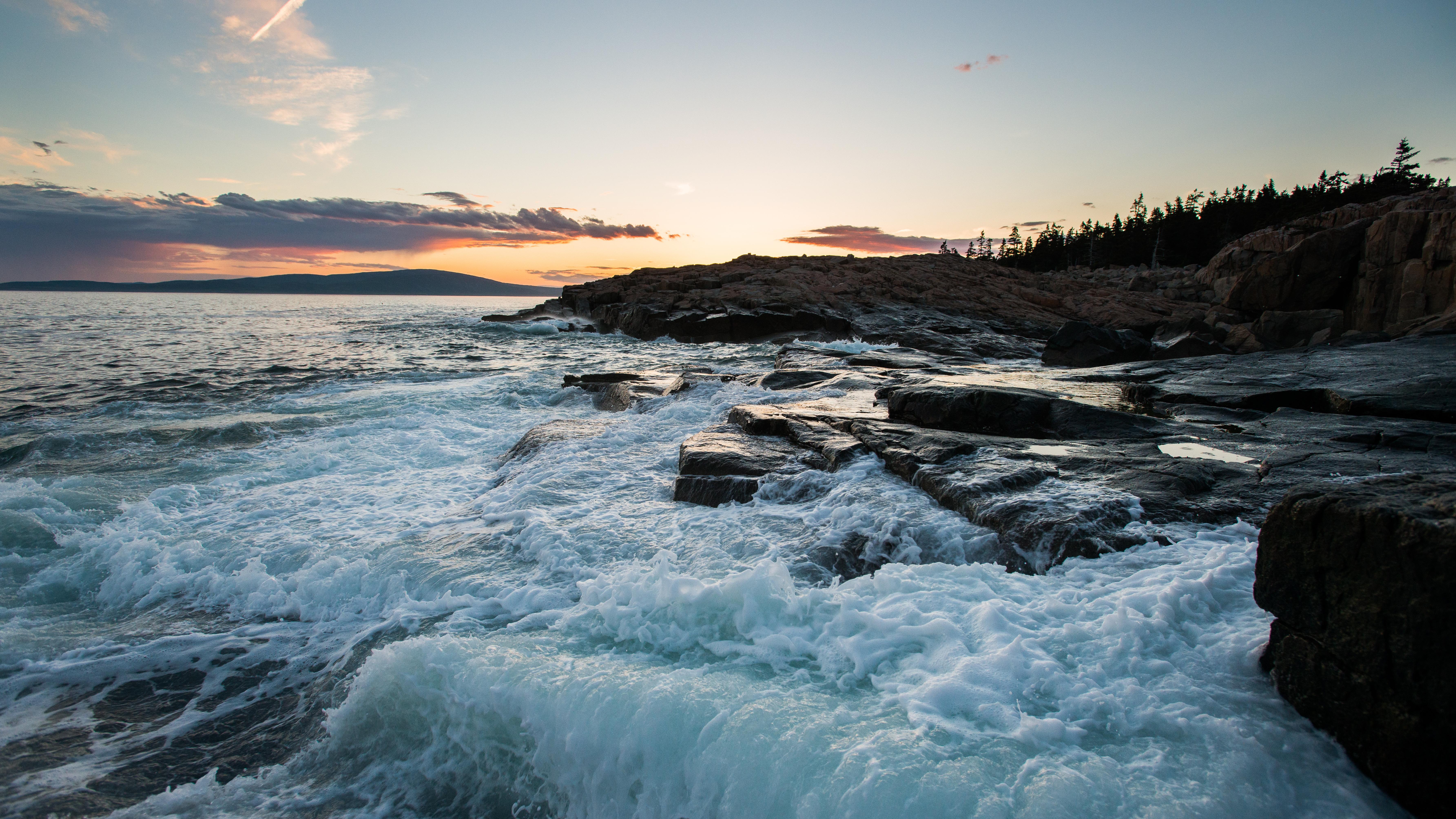 Waves crash against rocky coastline at sunset