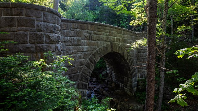 A stone carriage road bridge over a stream in a forested area