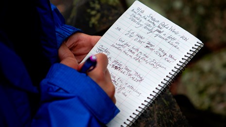 A person wearing a blue jacket writes in a notebook