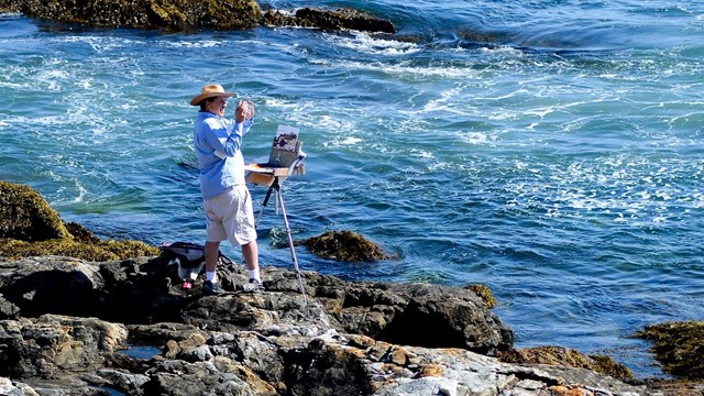 A painter uses a smartphone to snap a photo of the coastline