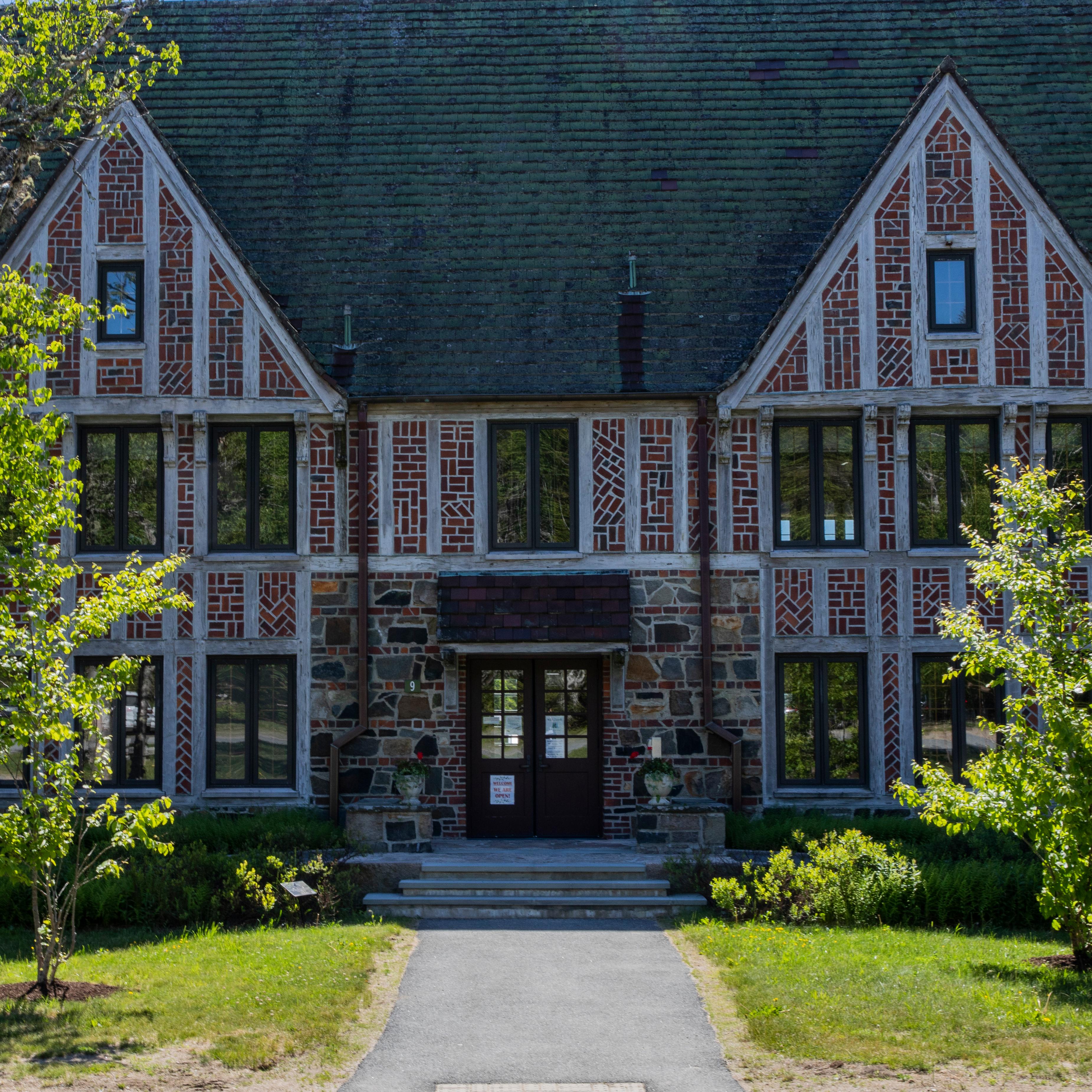 A two story brick building with trees on a lawn in front