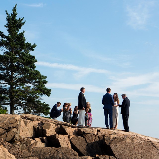 A bride and groom stand on a cliff with a small group of people