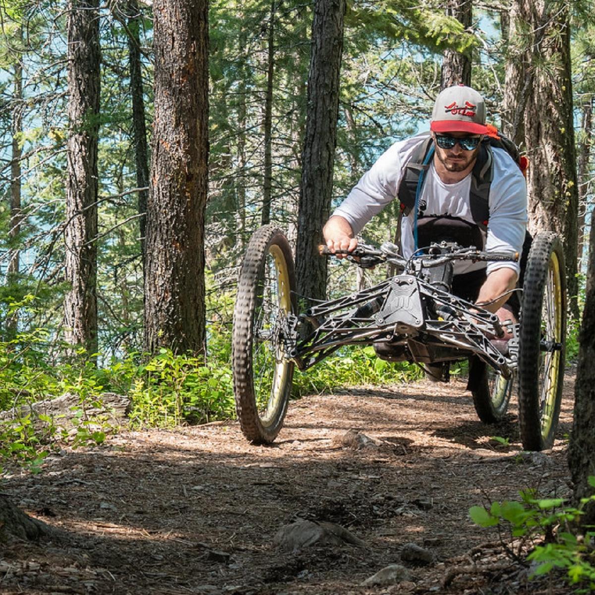 Man riding his off-road wheelchair through a pine forested trail.  