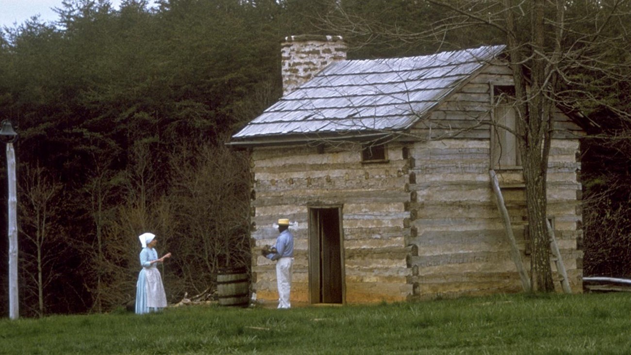 a rustic cabin with two individuals standing out front