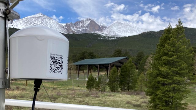 Close up of a PurpleAir sensor attached to a pole with mountains in the background