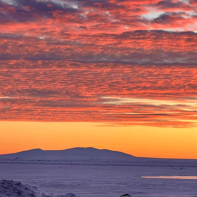 A deep orange sunset reflected on clouds above the Arctic.