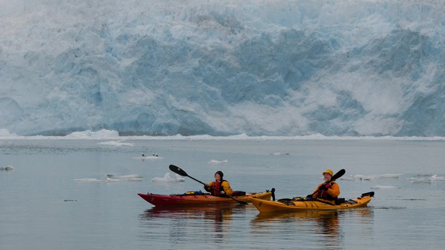 two kayakers paddle through icy waters near a glacier