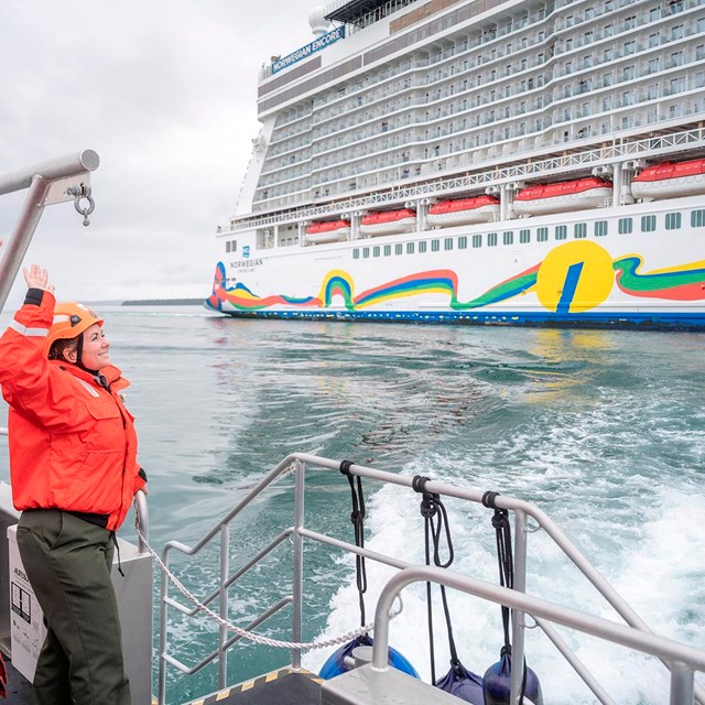 Rangers in bright orange jackets wave to cruise ship passengers.