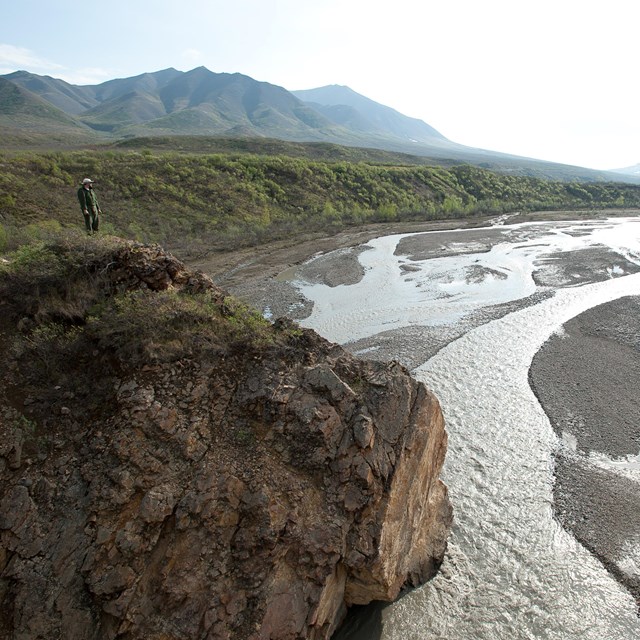 person standing on a bluff overlooking a wide braided river