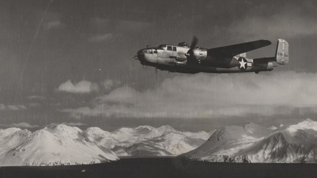 a historic image of two military planes flying high over a snowy coastal mountain range.