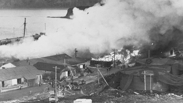 Black and white photo of a town with burning buildings and billowing smoke. 