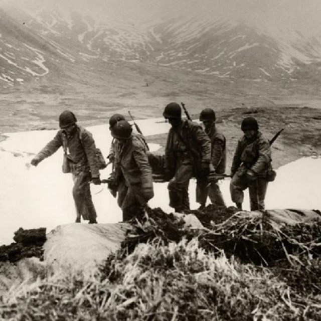 a historic scene of five soldiers carrying a litter with a person on it through mountainous terrain.