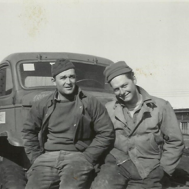 two men sit on the bumper of a truck