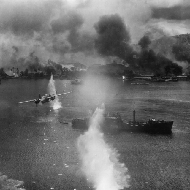 Plane flying over battleship with things exploding