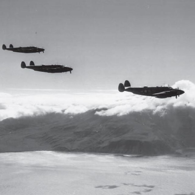 Black and white photo of three planes flying over ocean and mountains