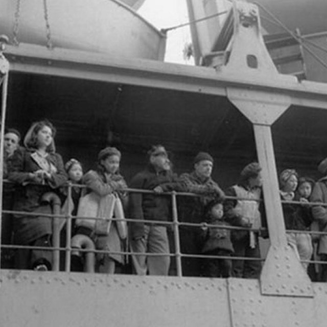 A historic scene of people lining the railing on a ship.