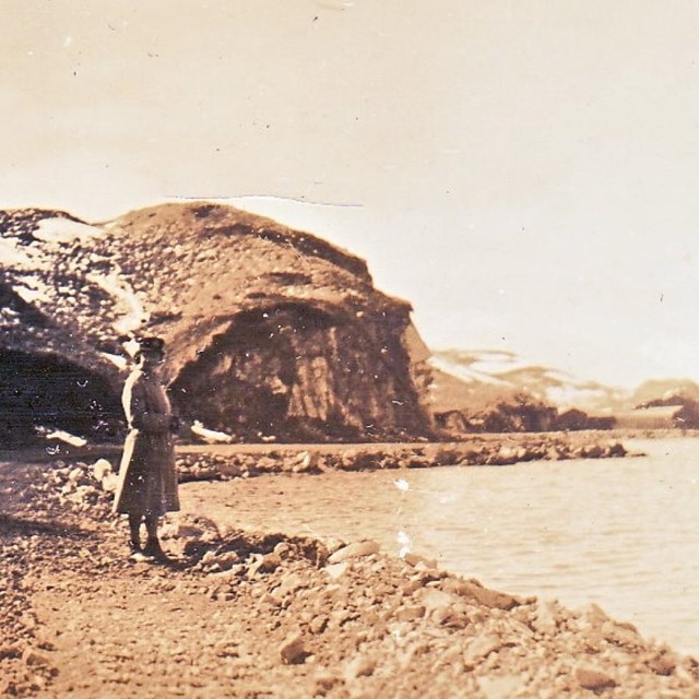 a historic scene of a person standing on a coastal dirt road with massive cliffs.