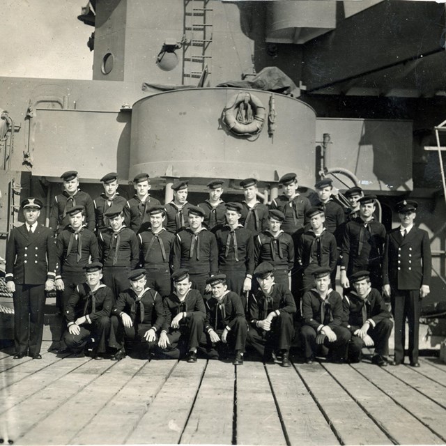 Three rows of uniformed sailors in front of a submarine