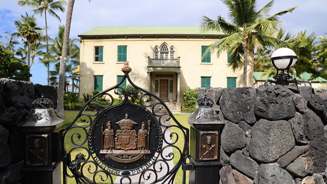 Historic palace behind an entrance gate with a traditional Hawaiian seal engraved in metal