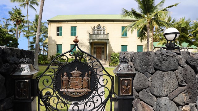 Historic building flanked by coconut trees behind a metal gate