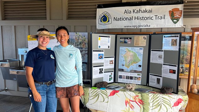 Pair of interns stand in front of an informational display about the Ala Kahakai