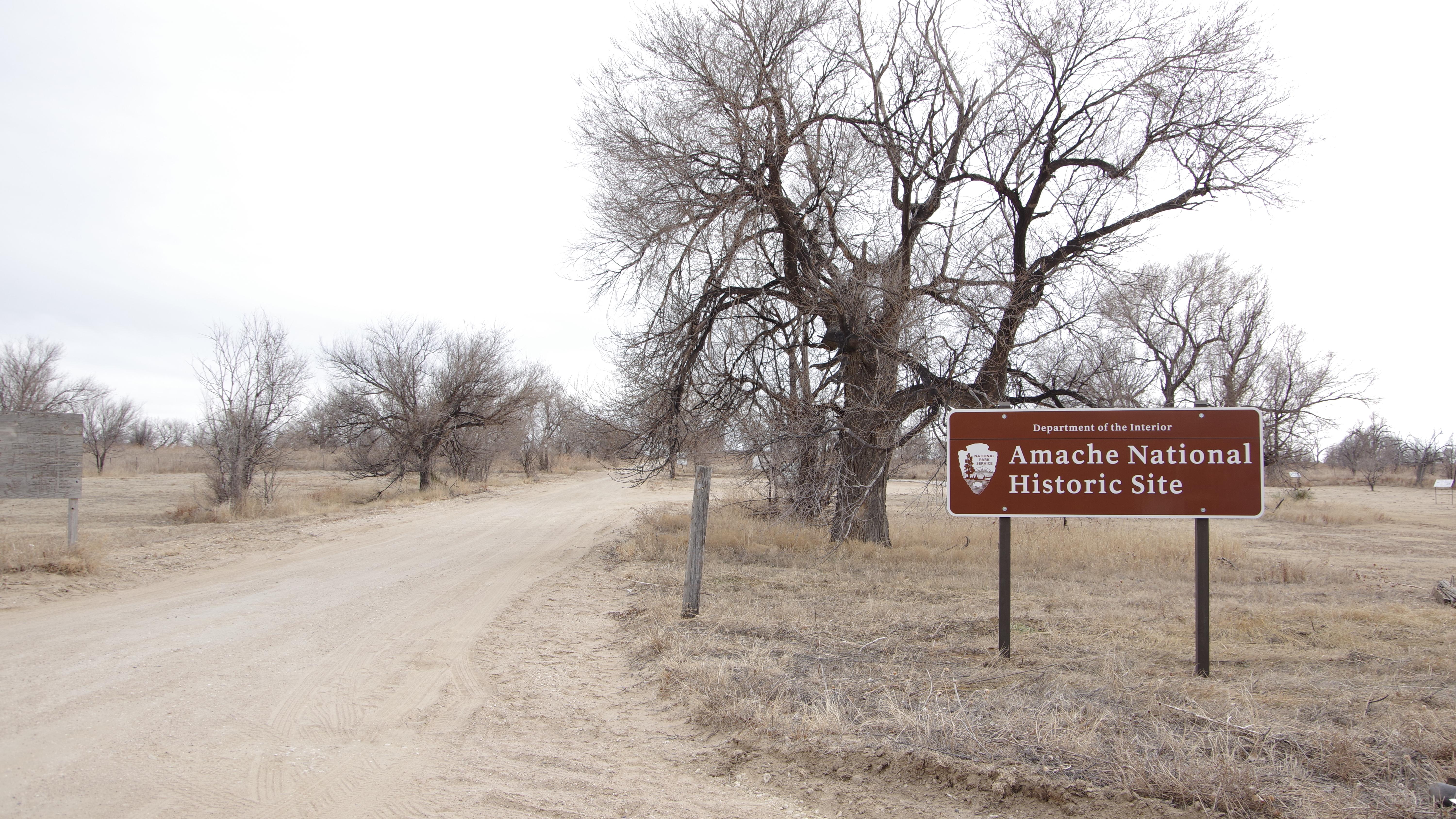 A brown sign reads "Amache National Historic Site" next to a gravel road.
