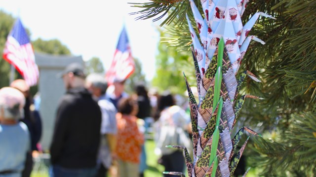A chain of origami cranes hangs from a tree in front of an out of focus crowd