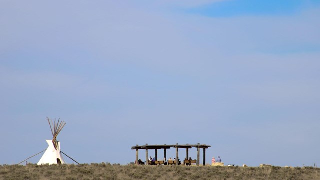 A tipi on top of a hill next to a shade structure