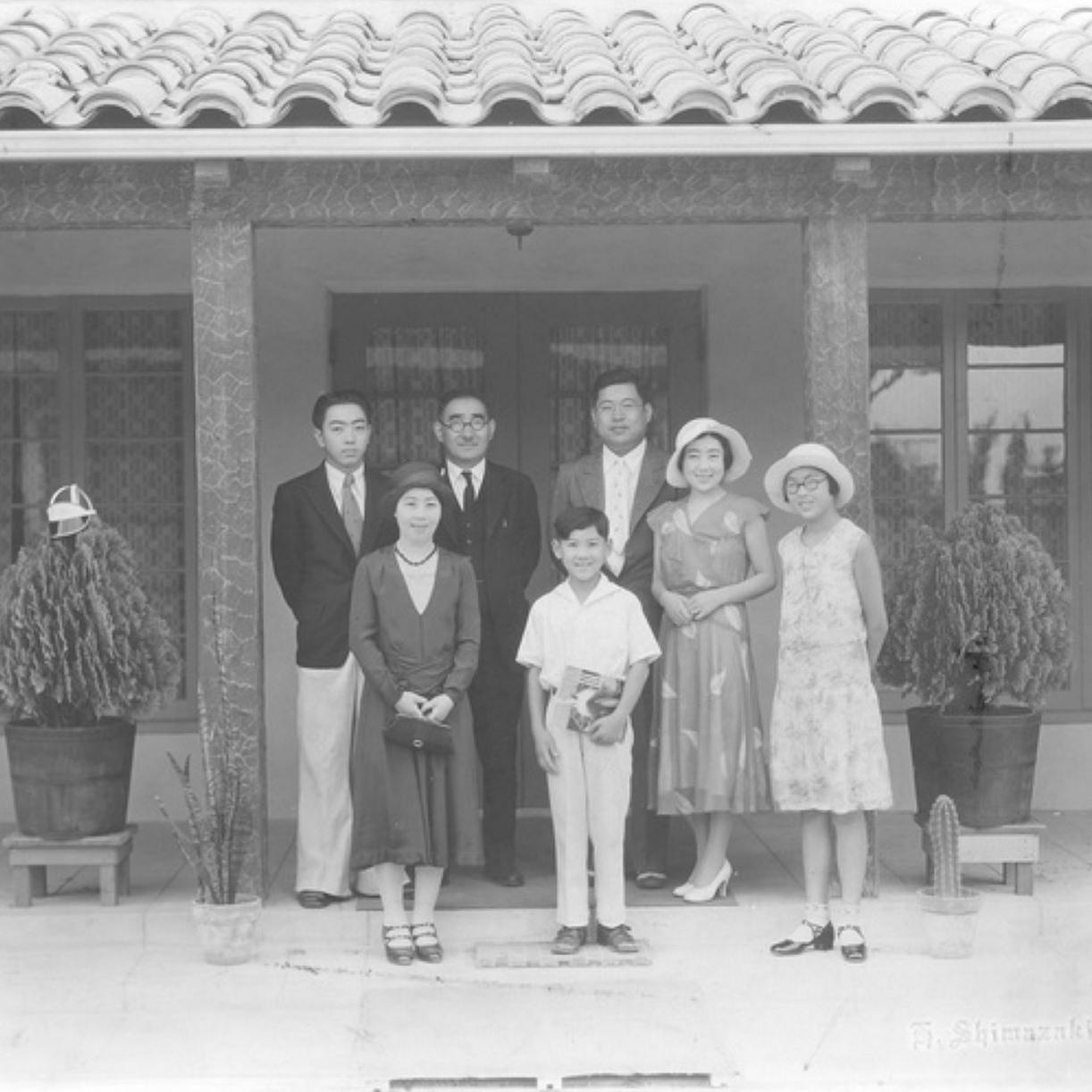 Seven people standing in front of a building. There are three men, two women, a girl and a boy.
