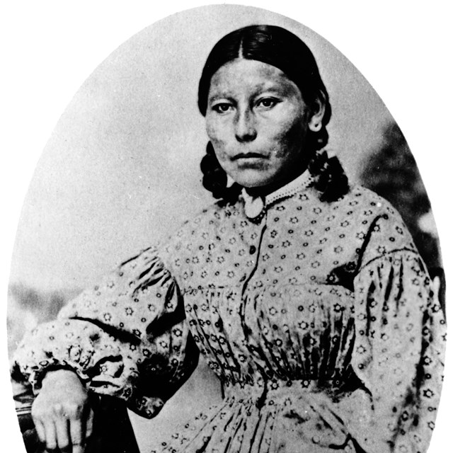 A historic photo of an indigenous woman in a high neck, long sleeved dress.