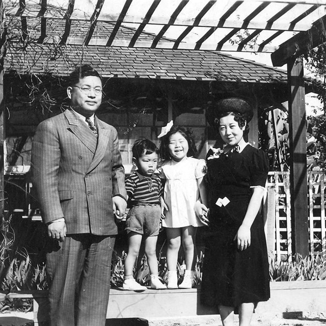 Black and white image of a family of four Japanese Americans standing in front of their house