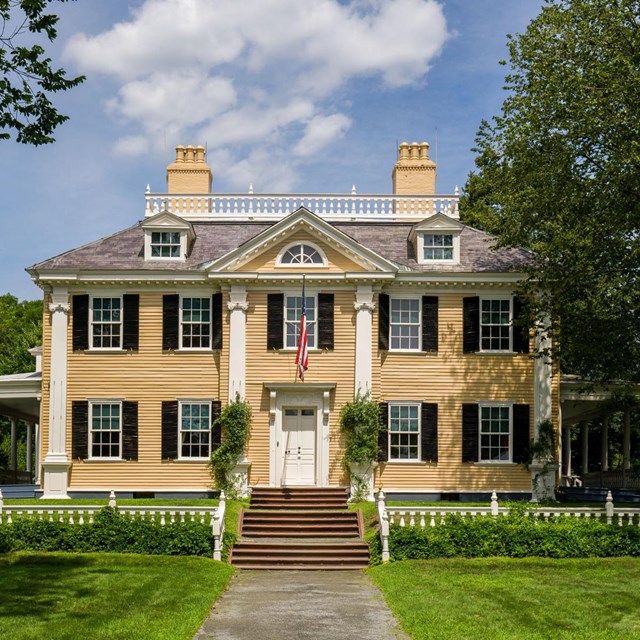A two-story yellow building with white columns set against a bright blue sky. 