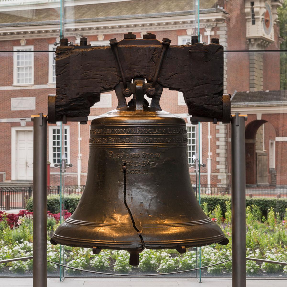 The Liberty Bell suspended between two posts. Independence Hall can be seen through the window.