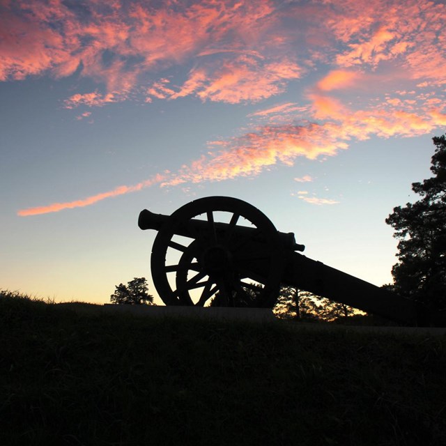 The silhouette of a cannon against the light blue sky with pink clouds