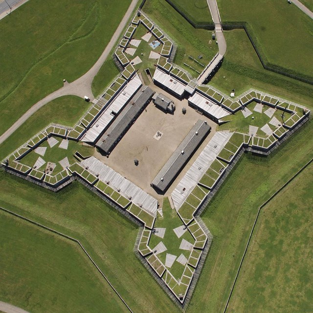 A view of the fort from above. A wooden star-shaped building sits in the middle of a grass field.