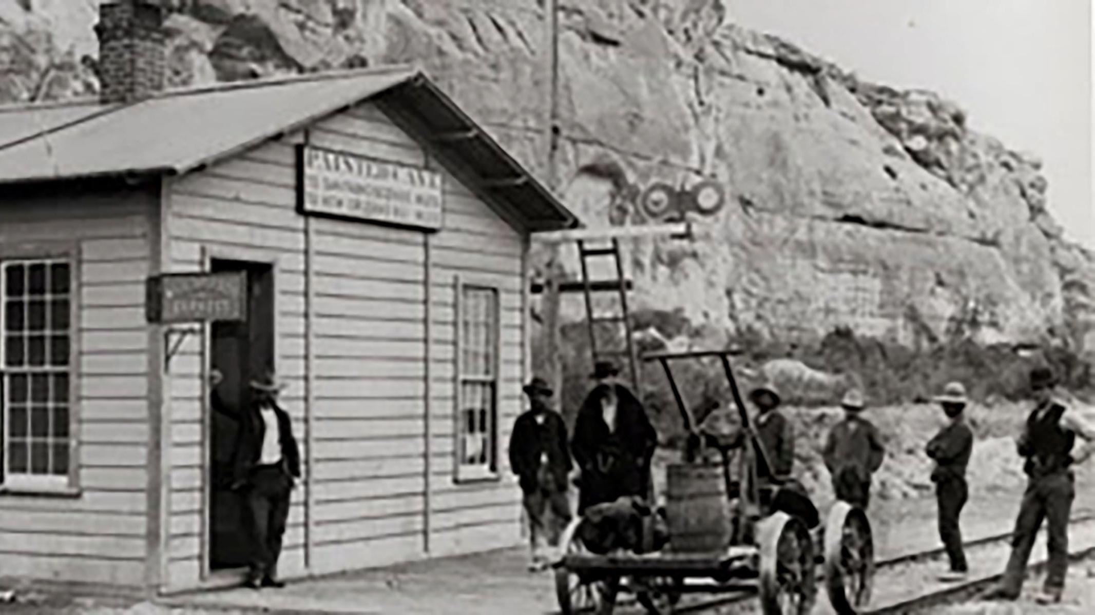 Old depot with men lolling around in front.