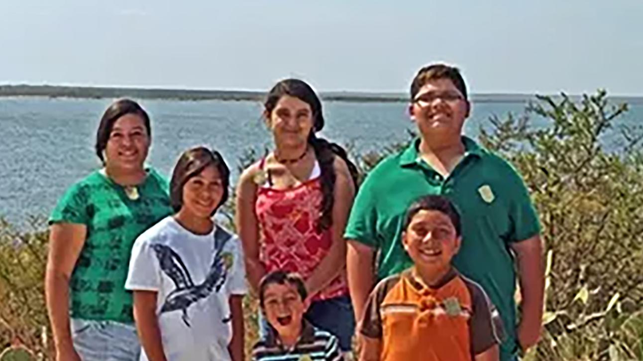 Jr Ranger family with 2 parents & 3 kids ranging from about 8-16 years old on shore of Lake Amistad 