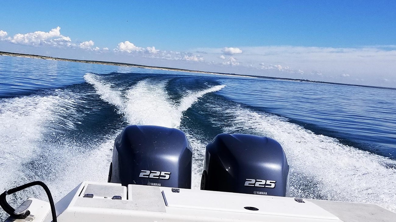 Image of motorboat stern making a sharp turn and wakes on a still, blue lake