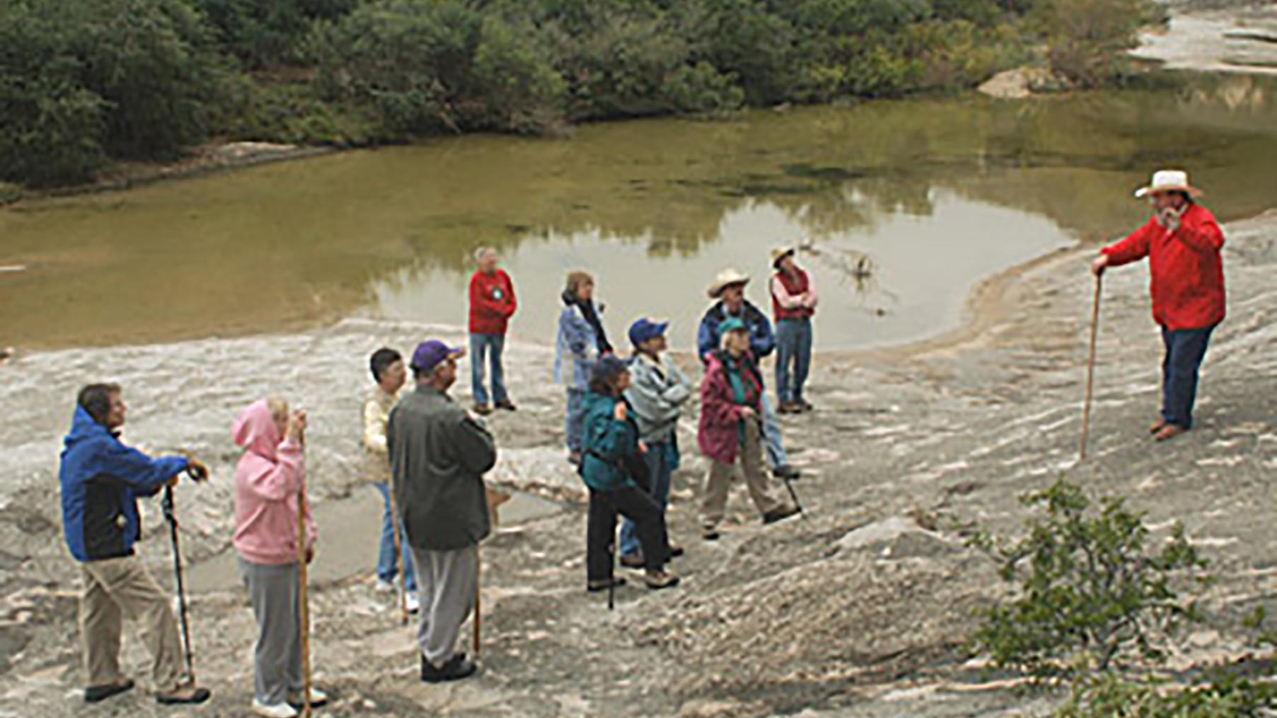 Tour group at riverbank with leader presenting information.