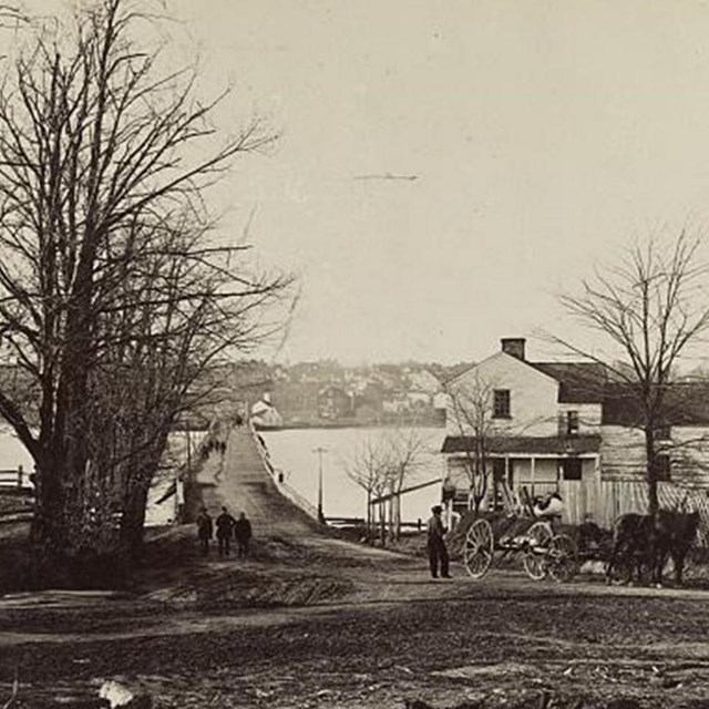 A bridge across a river with a small house and a tree.