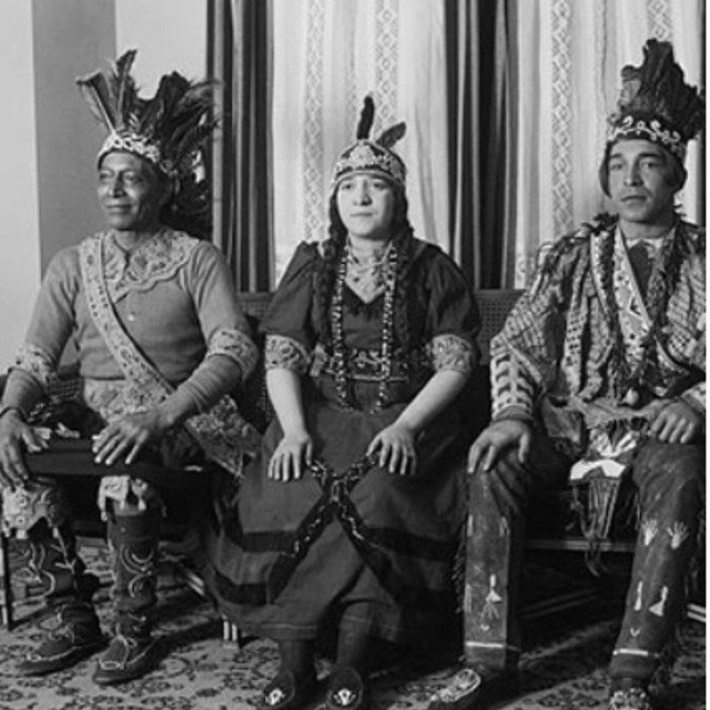 Three Native Peoples are shown sitting in chairs.