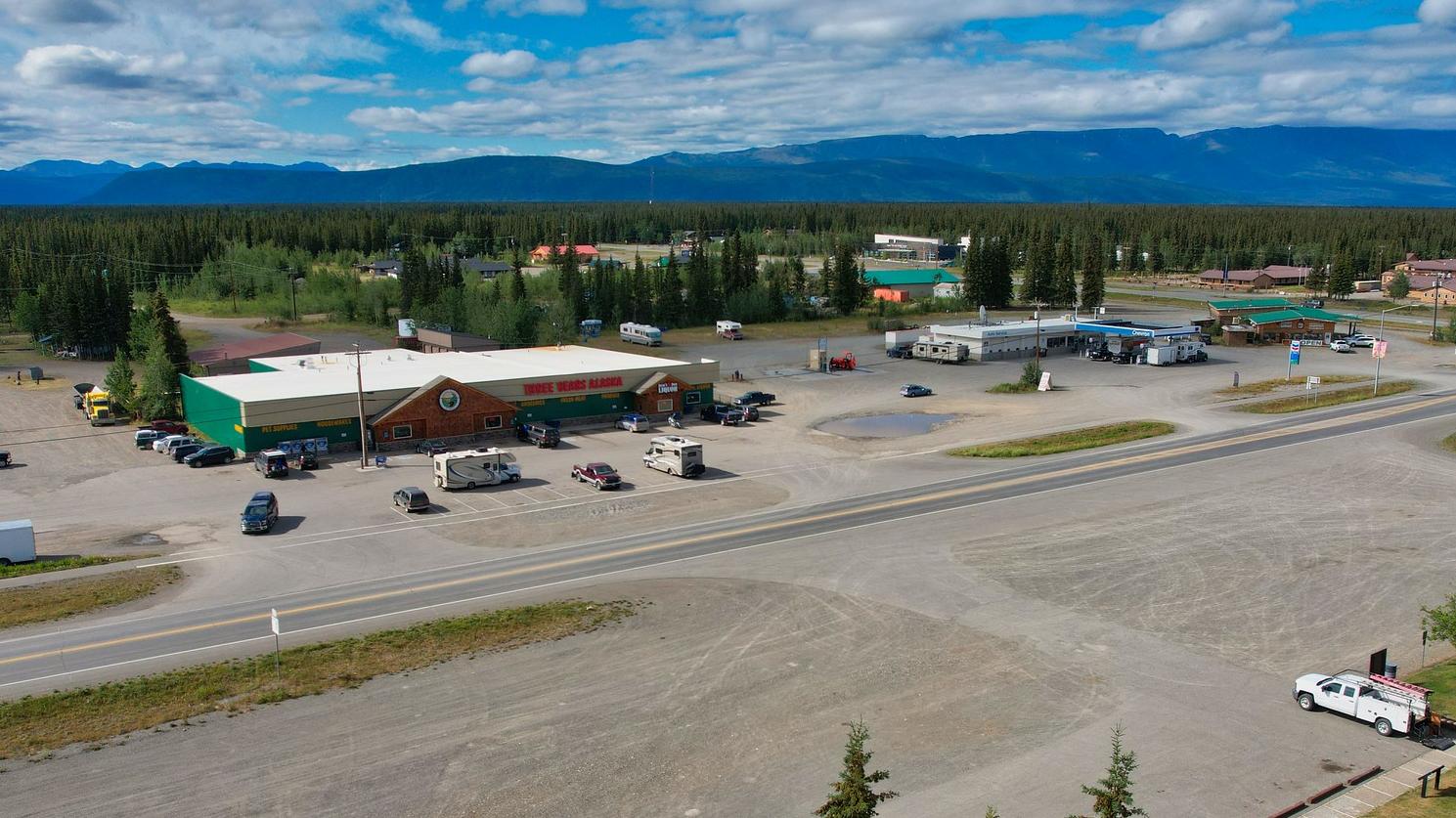 Birdseye view of a couple buildings and paved road with interspersed trees.