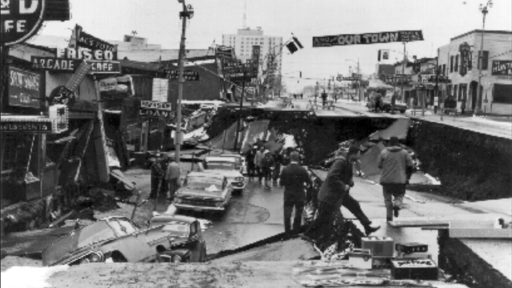 Collapsed street 11ft below street level; cars, people, and sidewalk in the collapsed area.