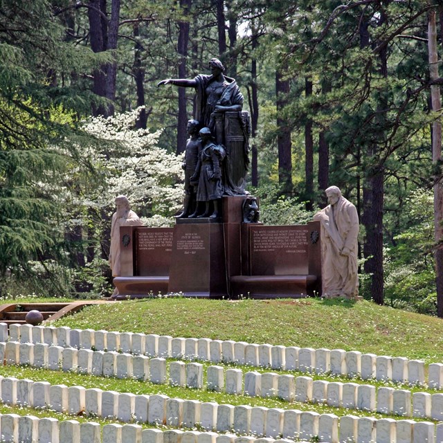 Monument featuring women, men and children surrounded by headstones. 