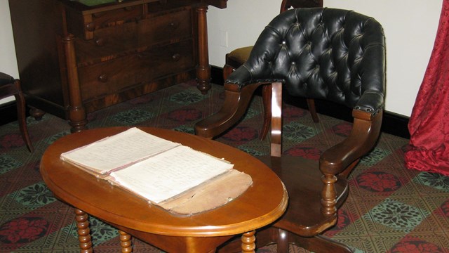Image of wheeled leather chair in front of a wooden table with documents spread out on top.