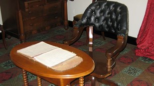 A leather chair pulled up to a wooden table with documents spread out on top.