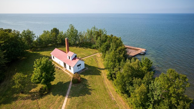 Photograph of a building from above with green grass grass, trees and a large lake on the horizon.