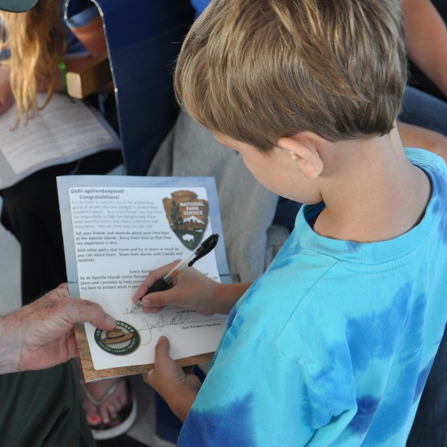 Young child signing a certificate with a park ranger.