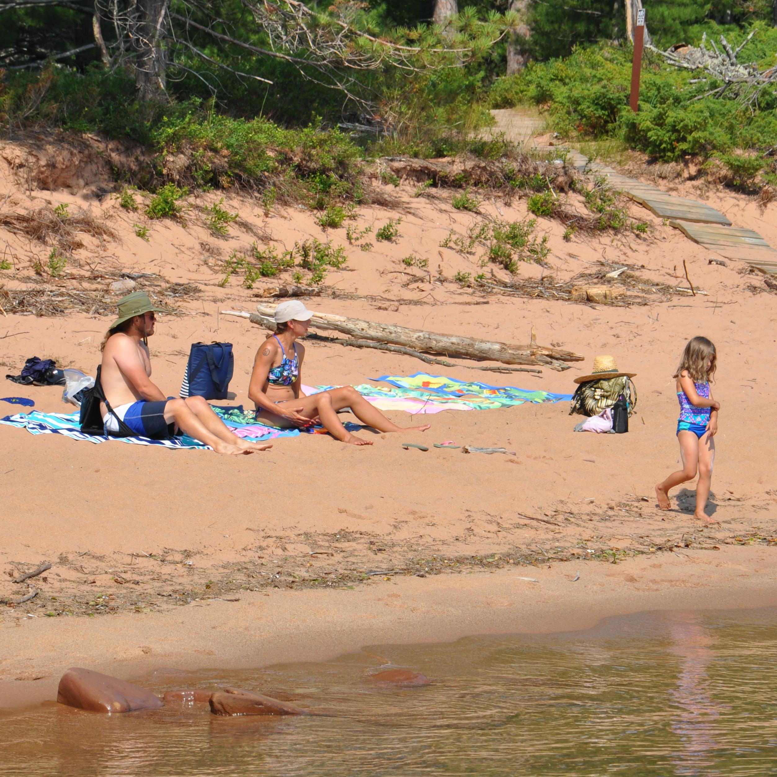 Family of 3 sitting on a sandy beach.