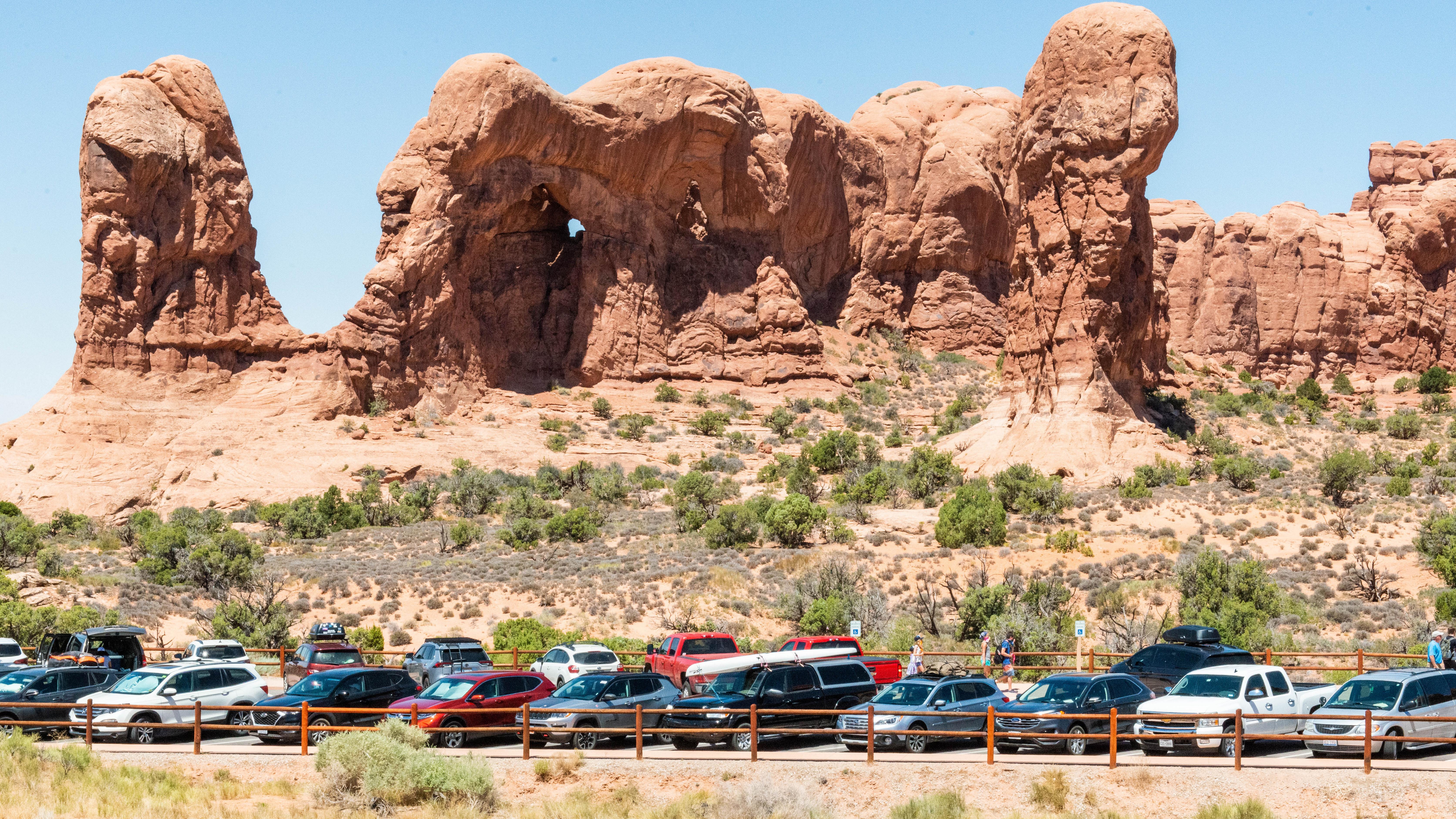 Cars parked in a lot in front of large sandstone formations